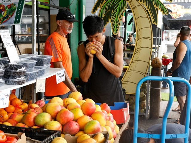 Shoppers at a market stall piled high with mangoes and stone fruit