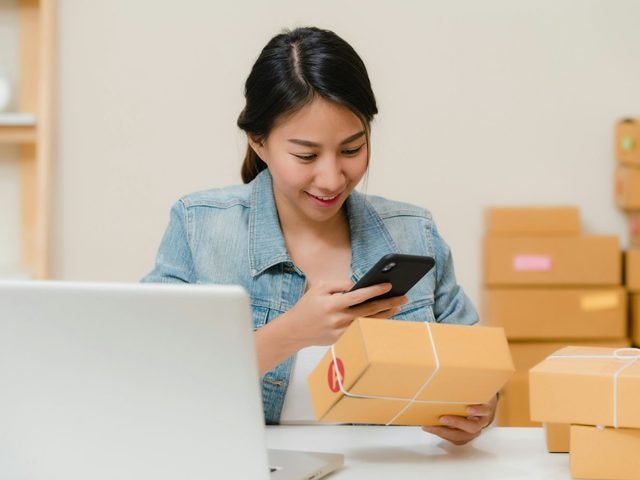 Small-business owner checking an order on her phone among parcels