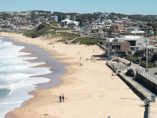 Sunny surf beach with a promenade and hillside suburbs behind