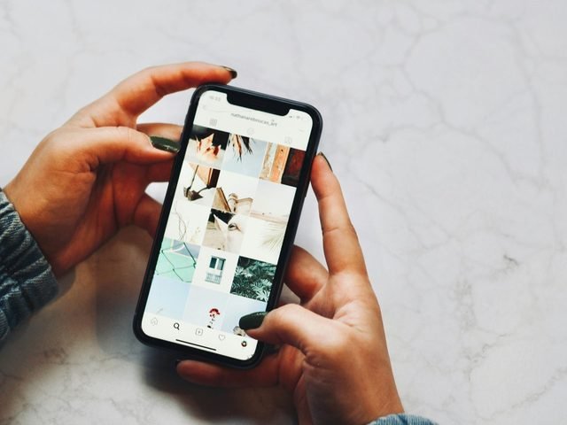 Hands holding a phone showing a grid of photos