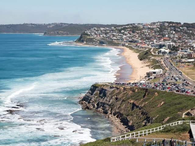 Aerial view of a surf beach, headland and coastal suburbs