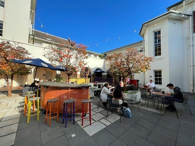 Busy courtyard café with colourful stools beside a heritage building on a sunny day